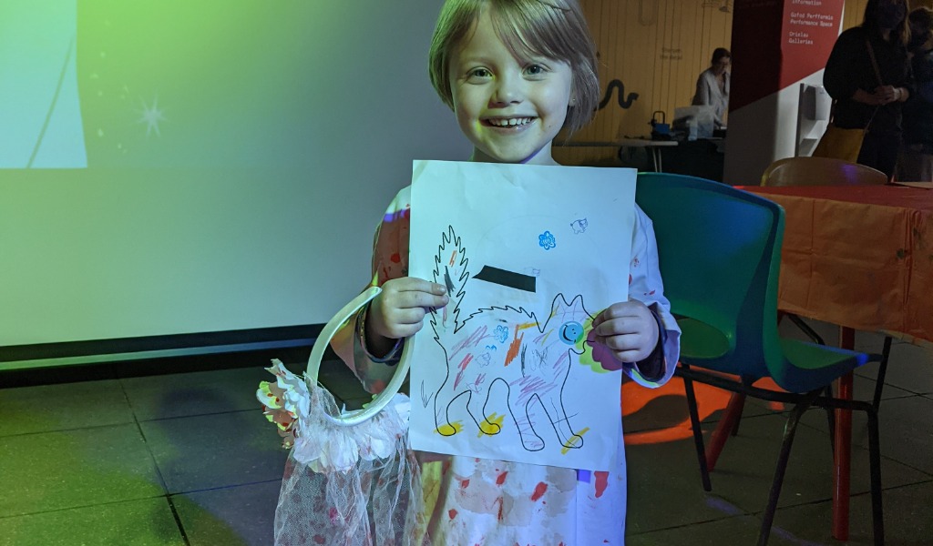 A child dressed as a zombie-bride shows us her collage of a spooky cat.